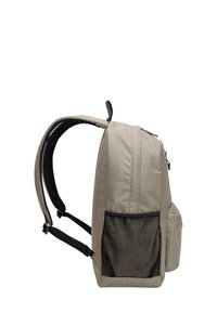 Sac à dos en tissu beige avec une poche latérale en mesh, des bretelles ajustables et une poignée supérieure. Il dispose d'une fermeture éclair et d'un design élégant et structuré.