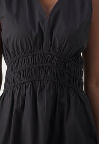 Svart ärmlös klänning med djup V-ringning, elastiskt midjeband och flödande kjol med en texturerad, rynkad tygdesign.