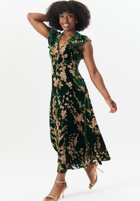 Velvet green dress with floral pattern, V-neck, short ruffles on sleeves, flowing silhouette, mid-calf length, paired with gold sandals.
