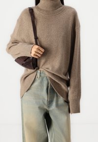 Maglione a collo alto lavorato a maglia marrone con polsini e orlo a coste, abbinato a jeans a vita alta blu chiaro, con un leggero schema di lavaggio.