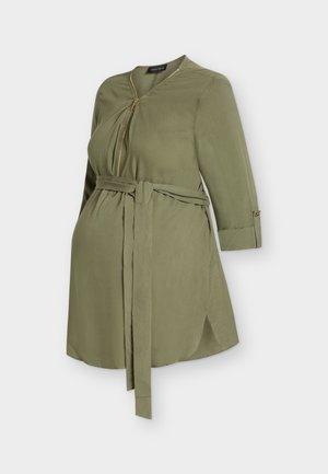 Μπλούζα εγκυμοσύνης σε ελιά πράσινο με φερμουάρ μπροστά, μακριά μανίκια με μανσέτες με κουμπιά και ζώνη στη μέση, άνοιγμα πλαϊνό στο κάτω μέρος.