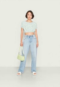 Blomsterprint crop top i lys grøn, løs pasform; højhælede lyseblå jeans; lys grøn taske; hvide slidesandaler.