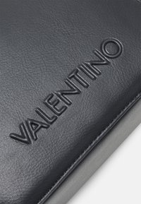 Black leather item featuring embossed "VALENTINO" text. Smooth texture with subtle shine, rectangular shape with clean edges.