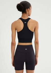 Czarny sportowy crop top z wycięciem na plecach, zestawiony z czarnymi szortami o wysokim stanie. Obie części mają małe logo na plecach.