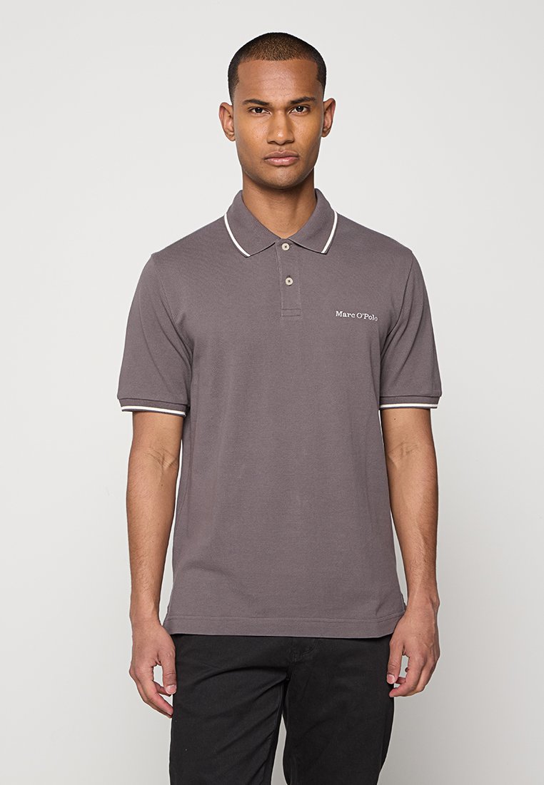 Mężczyzna stojący przodem, ubrany w szary podkoszulek Marc O'Polo z białymi wykończeniami przy kołnierzy i krawędziach rękawów.