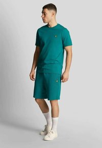 T-shirt in cotone turchese e pantaloncini abbinati, con un piccolo logo giallo, scollo rotondo e vestibilità comoda, abbinati a calzini bianchi e sneakers.