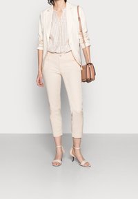 Blazer beige combinado con una camisa clara de cuadros, pantalones crema y sandalias de tacón nude. Bolso bandolera en rosa suave con cadena.