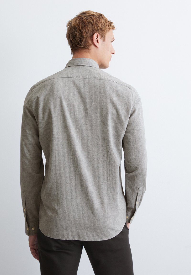 Grau gestreifte Button-Up-Bluse mit Kragen und langen Ärmeln. Verfügt über goldene Knöpfe und einen abgerundeten Saum. Getragen mit dunklen Hosen.