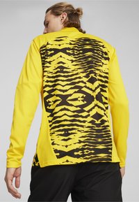 Giacca atletica a maniche lunghe con un vivace davanti giallo e un motivo geometrico nero sul retro, realizzata in tessuto leggero.