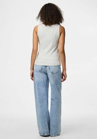 Graues ärmelloses Oberteil, kombiniert mit hellblauen, weit geschnittenen Jeans. Der Stoff sieht weich aus; die Jeans haben klassische Gesäßtaschen und eine ausgewaschene Optik.