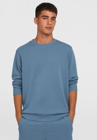 Lyseblå sweatshirt lavet af blødt stof, med rund halsudskæring, ribstrikkede manchetter og et diskret logo på brystet. Casual pasform og glat tekstur.