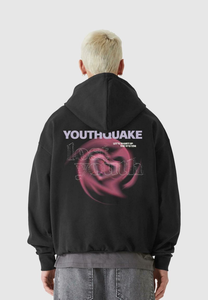 Svart huvtröja med en grafisk tryck på baksidan. Texten säger "YOUTHQUAKE" med abstrakta rosa virvlar. Mjuk textur.