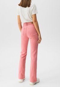 Jean flare rose avec taille haute, deux poches arrière et détails de couture subtils. Associé à un t-shirt blanc et des baskets blanches.