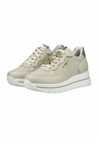 Baskets beige avec semelles blanches, texture en mesh et cuir, œillets dorés, et ornements en forme de gemme verte sur les lacets, présentées côte à côte.