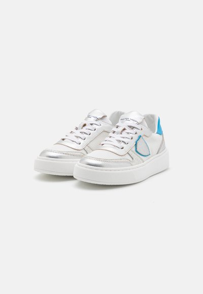 Weiße Turnschuhe mit silbernen Akzenten, strukturiertem Stoff und einer hellblauen Fersenlasche. Mit Schnürverschluss und robuster Gummisohle.