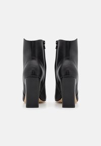 Bottines en cuir noir avec une texture lisse, hauts talons compensés et fermeture par zip sur le côté. Design épuré, bords lisses et détails minimaux.