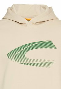 Beżowa bluza z kapturem z dużym zielonym paskowanym logo z przodu, z stylizowanym wzorem litery "C". Dekolt posiada kieszeń kangurzą poniżej.