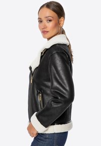 Czarna skórzana kurtka z puszystym białym kołnierzem i mankietami z owczej wełny, z zamykanymi na zamek kieszeniami i złotymi akcentami.