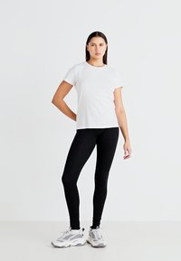 Hvit t-skjorte med korte ermer kombinert med svarte leggings og grå joggesko. Glatt stoff med et enkelt design og figurtilpasset silhuett.