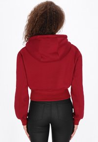 Sudadera roja corta con capucha ajustable, bolsillo frontal estilo canguro y mangas oversize. Tela suave con bajo y puños acanalados.