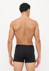 Schwarze Boxershorts mit glatter Textur und elastischem Bund, von hinten betrachtet, die ein enganliegendes Design und minimale Nähte zeigen.