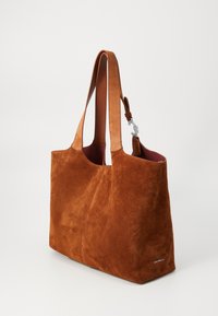 Ruda od suede petnešinė rankinė su tekstūruotomis odinėmis diržais, atvira viršuje ir tamsiu interjeru. Savybė – mažas sidabro spalvos aksesuaras ir logotipas.