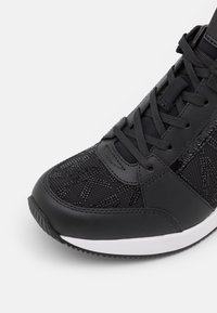 Gros plan d'une basket noire avec des détails en mesh et cuir, des lacets noirs, une semelle blanche et un logo sur le panneau latéral.
