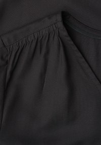 Gros plan sur l'épaule d'un vêtement noir avec tissu froncé et couture visible près d'un col arrondi.