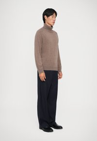 Brown turtleneck sweater made of soft material, paired with loose navy pinstriped trousers. The outfit features long sleeves and a fitted collar.