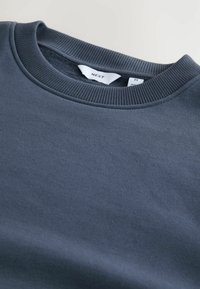 Donkergrijze sweatshirt met een geribbelde ronde hals en een zachte textuur. Label zichtbaar binnen de kraag. Eenvoudig, ongecompliceerd ontwerp.