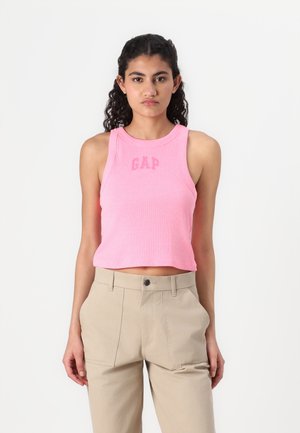 Vaaleanpunainen lyhyt tanktoppi ribatusta kankaasta, jossa on vaaleamman vaaleanpunaisen "GAP"-logo, yhdistettynä korkeavyötäröisiin beigeihin housuihin, joissa on sivutaskut.