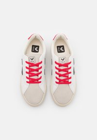 Białe sneakersy z czerwonymi sznurówkami i ciemnogranatowymi akcentami, z teksturowanym szarym noskiem i logo "VEJA" na języku. Gumowa podeszwa.