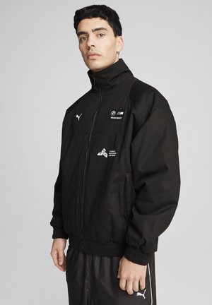 Black jacket with a high collar, front zipper, ribbed cuffs and hem. Features BMW and Puma logos on chest and left sleeve. Smooth texture.