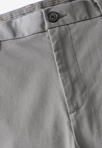 Pantalons en tissu gris avec une surface texturée, dotés d'une fermeture à bouton supérieur et de poches latérales pour plus de praticité.