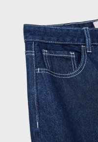 Denimske hlače temno modre barve, ki imajo klasičen dizajn s petimi žepi, kontrastno belo šivanje in trden pas z zankami za pas.