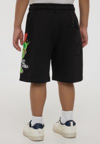 Pantaloni corti neri in cotone con vita elastica e tasca sul retro. Presentano un design grafico colorato sulla gamba sinistra con del testo.