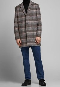 Cappotto a quadri in tonalità grigie, nere e rosa con colletto e due tasche frontali; indossato su un dolcevita nero e jeans blu.