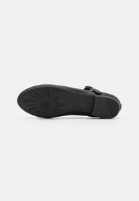 Suela de zapato negra con un patrón floral texturizado, presenta un diseño plano y un borde liso. Incluye un pequeño tacón y una correa ajustable con hebilla.