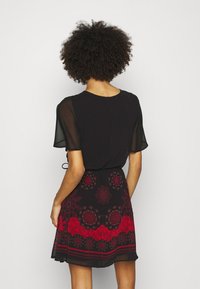 Černé šaty s průsvitnými krátkými rukávy, květovaným červeno-černým vzorem na lemu a detailem vázání v pase. Lehká látka, střih do áčka.