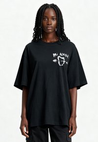 T-shirt noir surdimensionné en coton avec des manches courtes, présentant un graphique imprimé blanc sur le devant avec l'inscription "Mi Amor."