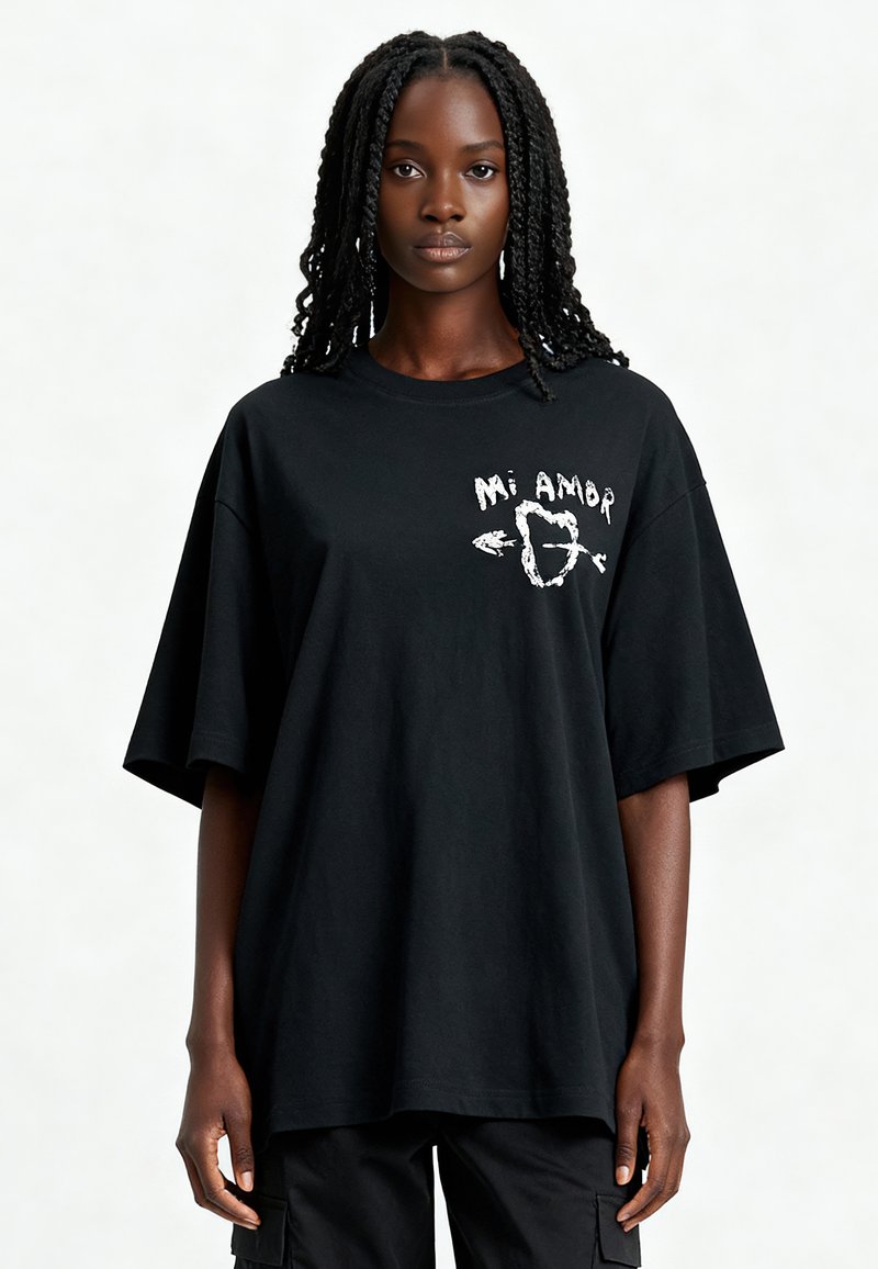 T-shirt noir surdimensionné en coton avec des manches courtes, présentant un graphique imprimé blanc sur le devant avec l'inscription "Mi Amor."