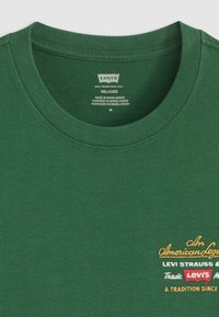 Groene katoenen T-shirt met een ronde hals. Voorzien van geborduurde tekst in het geel en rood, die het merk en de erfgoed van Levi's benadrukt.