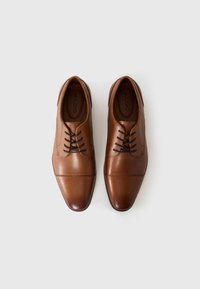 Zapatos de vestir de cuero marrón con punta redonda, que cuentan con cordones, costuras rectas y una textura suave. Logotipo de la marca visible en el interior.