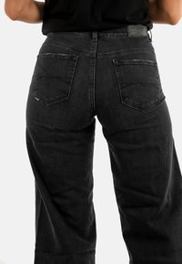 Jeans de mezclilla negra de pierna ancha con una cintura alta, bolsillos traseros, detalles de costura sutiles y una etiqueta de tela en la cintura.