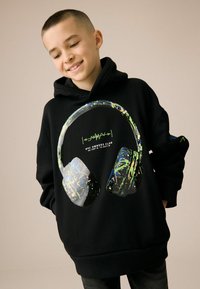 Zwarte hoodie met een grote grafische afbeelding van koptelefoons, aangevuld met kleurrijke spetterontwerpen en groene tekst. Zacht materiaal en een relaxed fit.