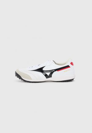 White athletic shoe with black accents, textured toe cap, rubber sole, padded collar, and red branding. Features a lace-up closure and streamlined design.
