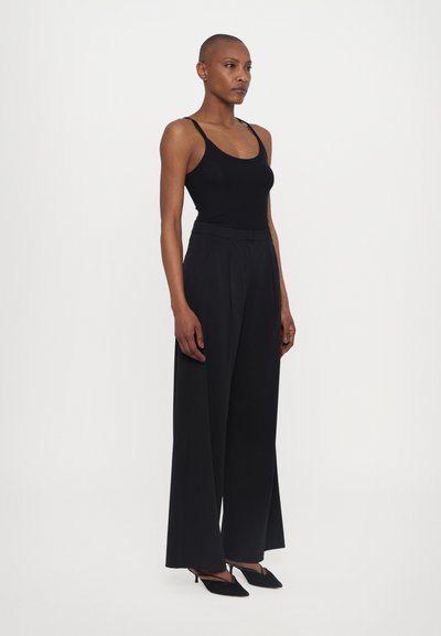 Melns bezpiedurkņu topiņš ar šauru piegriezumu, kombinēts ar augsto vidukli, platām melnām biksēm un norādītām melnām kurpēm ar augstu papēdi. Gluda auduma tekstūra.