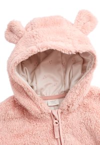 Sweat à capuche pour bébé rose et duveteux avec oreilles d'ours, fermeture à glissière complète à l'avant, et une doublure intérieure douce ornée d'un motif de pattes roses claires. Étiquette visible à l'intérieur.