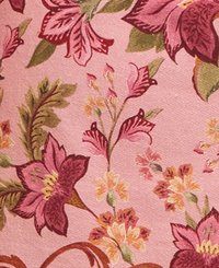 Tissu à motif floral avec un fond rose, présentant des fleurs violettes et jaunes, des feuilles vertes et des accents bruns en spirale. Texture lisse.