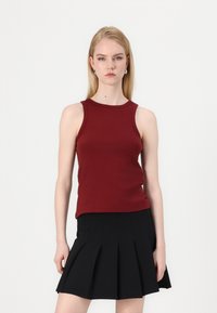 Burgundy ribbed tank top with a round neckline, paired with a black pleated mini skirt. Simple design, fitted shape, and smooth texture.